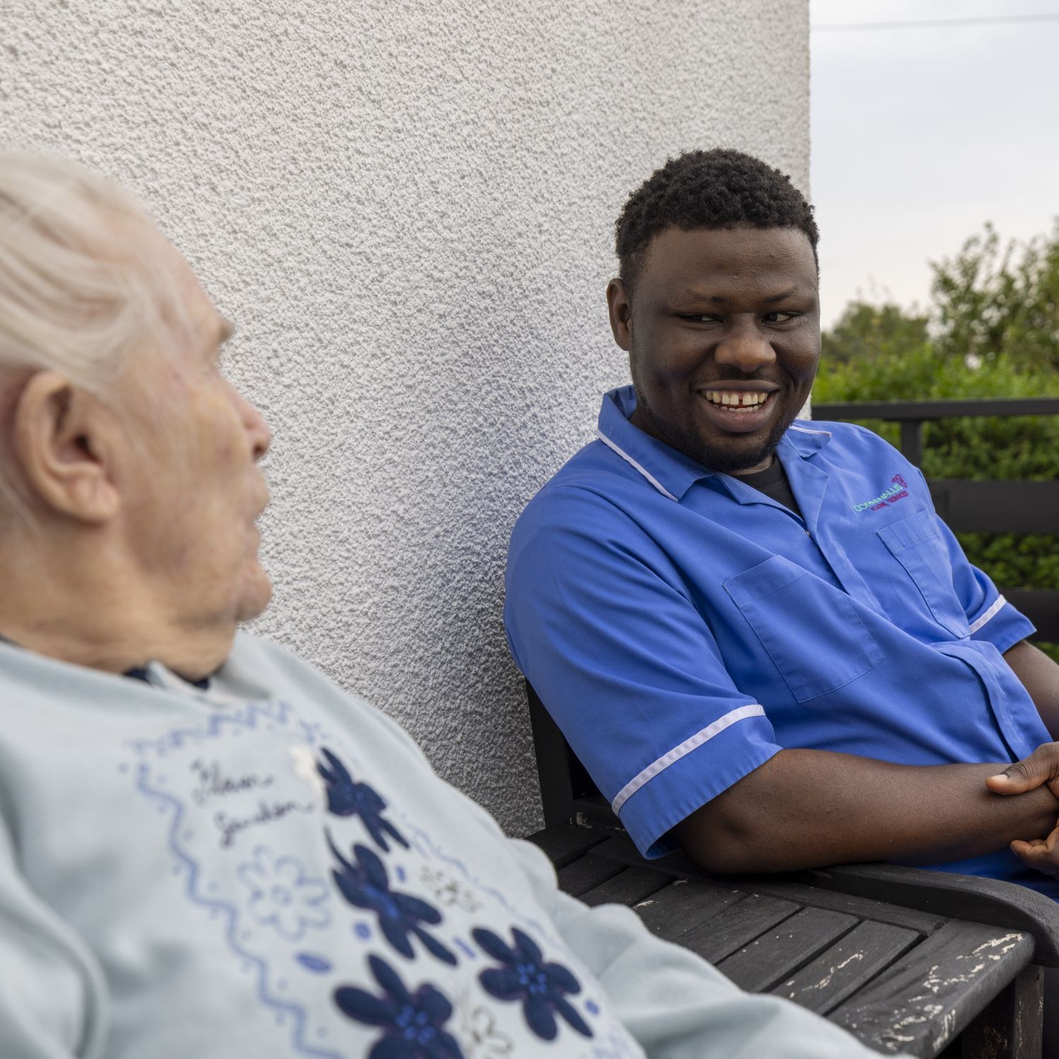 An elderly person sitting outside with a care professional
