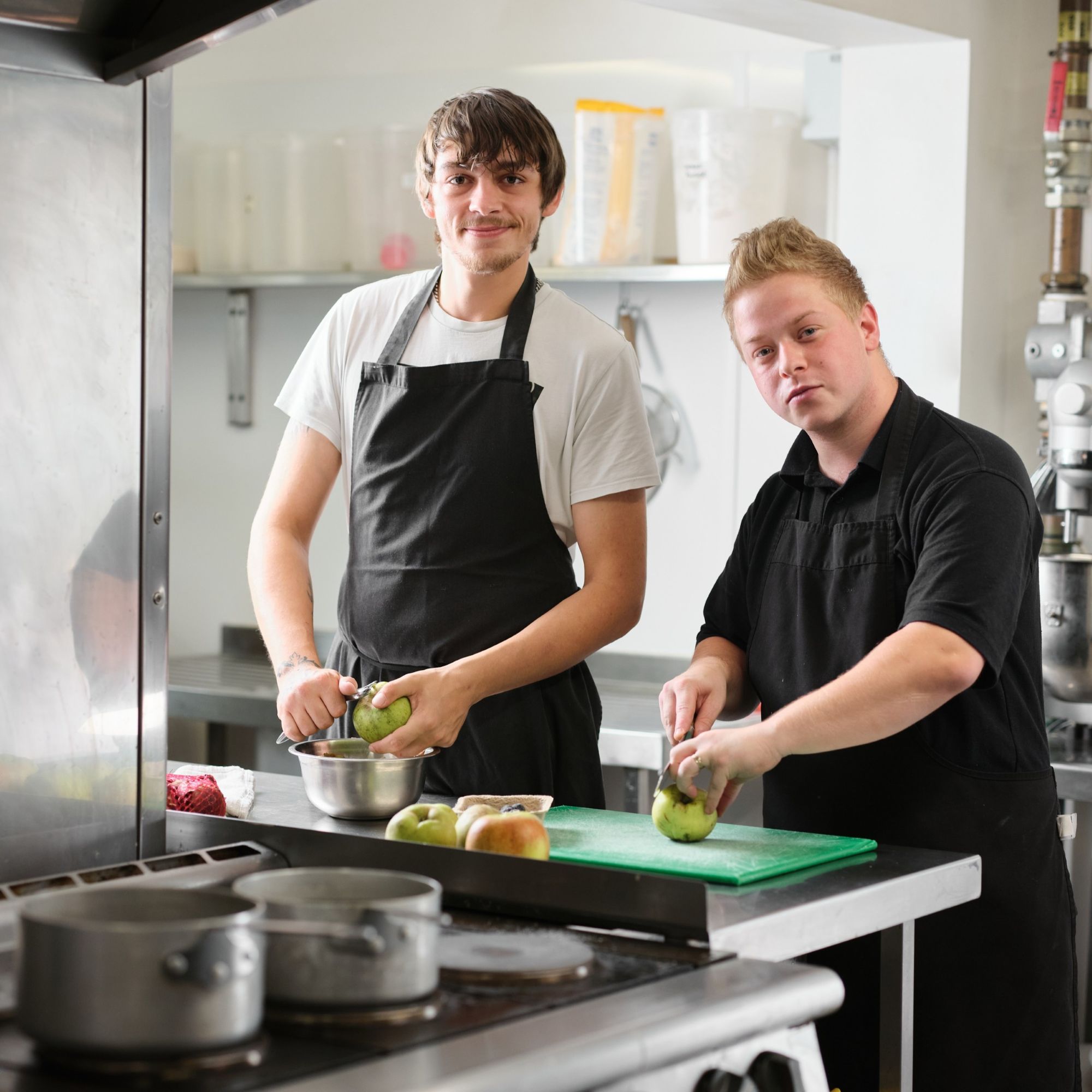 Two young men peeling apples in a kitchen